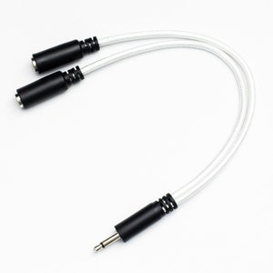 Puede incluir: Cable de audio blanco con dos conectores hembra de 3,5 mm en un extremo y un solo conector macho de 3,5 mm en el otro extremo.