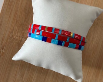 May include: Three stacked bracelets made of colorful square tiles. The bracelets are red, blue, and turquoise with gold accents.
