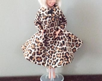 May include: A doll wearing a brown and white leopard print coat with a large collar.