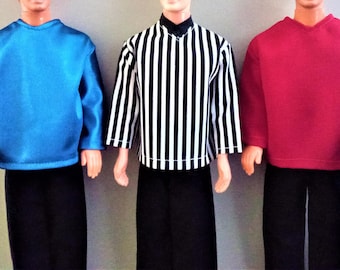 May include: Three doll outfits: a blue long-sleeve shirt, a black and white striped shirt, and a red long-sleeve shirt. Each shirt is paired with black pants. The outfits are displayed on dolls.