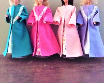 May include: Four dolls standing in a row, each wearing a long-sleeved, floor-length coat in teal, hot pink, light pink, or purple. Each coat features a white lace trim along the front opening and collar, worn over a patterned dress.