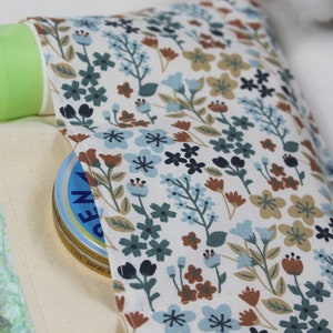 May include: A white canvas bag with a floral print lining. The bag is filled with baby supplies, including a green bottle, a blue pacifier, and a white jar of cream.