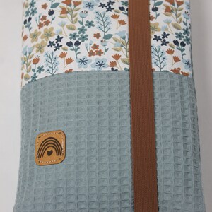 May include: A blue and white floral fabric pouch with a brown strap and a brown leather patch with a rainbow and heart design.