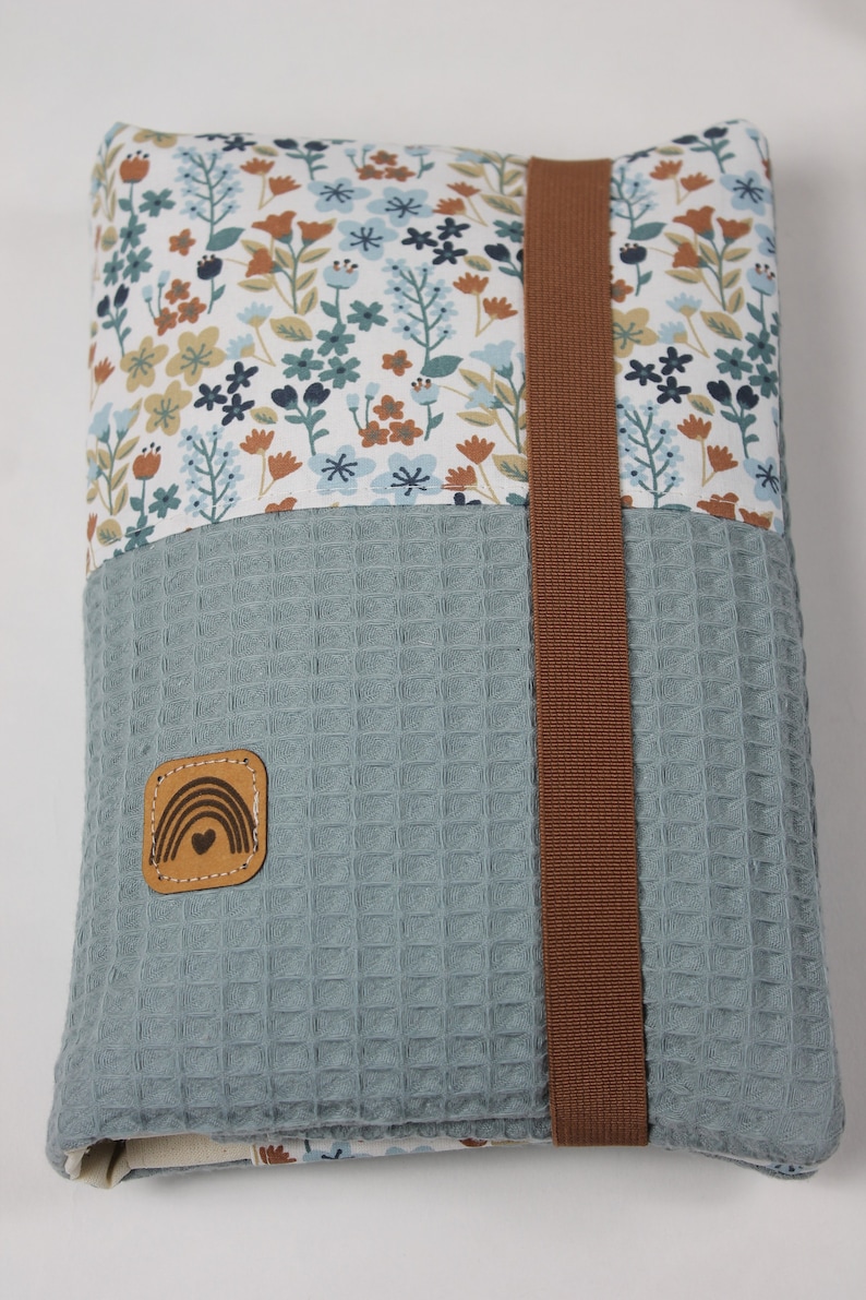 May include: A blue and white floral fabric pouch with a brown strap and a brown leather patch with a rainbow and heart design.