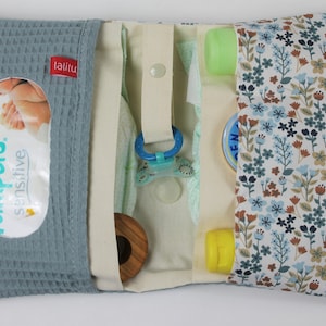 May include: A blue and white diaper bag with a floral pattern. The bag has a zippered closure and a flap with a snap closure. The bag is open and shows the inside, which is lined with a cream-colored fabric. The bag contains a variety of baby items, including diapers, wipes, a pacifier, and a bottle of lotion. The bag also has a small pocket on the outside for a phone or keys.