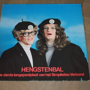 Peut inclure: Une pochette d'album de disque vinyle vintage représentant deux personnes portant des costumes et des chapeaux noirs. L'album est intitulé "Hengstenbal" et le texte ci-dessous indique "De derde langspeelplaat van het Simpliesties Verbond".