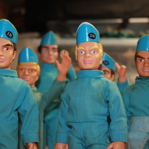 Op de afbeelding: Een groep blauwe en witte speelgoedfiguren die blauwe hoeden dragen met de letters 'IR' erop. De figuren dragen blauwe jumpsuits en hebben verschillende gezichtsuitdrukkingen.