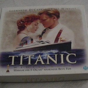 Könnte beinhalten: Ein weißes DVD-Gehäuse mit einem Bild von Leonardo DiCaprio und Kate Winslet aus dem Film Titanic. Das Gehäuse trägt den Titel "Titanic" in großen, weißen Buchstaben und den Text "Gewinner von II Oscars" in kleineren Buchstaben.