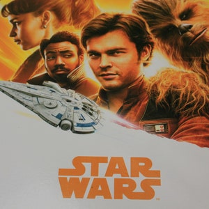 Könnte beinhalten: Ein Star Wars-Poster mit einem Raumschiff, einem Wookiee und drei Charakteren. Das Poster hat einen weißen Hintergrund mit orangefarbenem Text, der "STAR WARS" lautet.