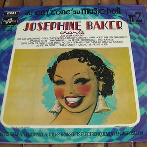 Puede incluir: Una portada de disco de vinilo vintage con Josephine Baker, una famosa cantante y bailarina, con el título "Josephine Baker chante" y el texto "du caf conc'au music-hall" en letras azules y blancas. La portada presenta una ilustración colorida de Josephine Baker con una gran sonrisa y grandes pendientes.