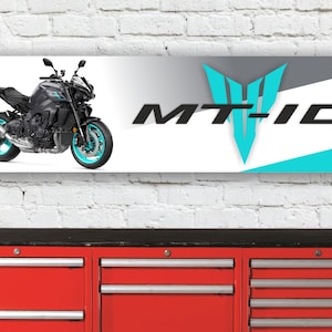 Può includere: Banner con una moto Yamaha MT-10 nera e turchese. Il banner presenta il logo MT-10 in nero e turchese. Lo sfondo è bianco, grigio e turchese. Il banner è esposto su un muro di mattoni bianchi.