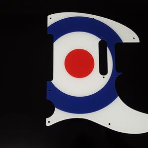 May include: A guitar pickguard in a target design, featuring white, blue, and red colours. The pickguard has a white base, a blue ring, and a red central circle. It has a distinctive shape with several holes.