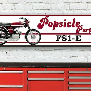Könnte beinhalten: Ein rotes und verchromtes Yamaha-Motorrad mit dem Text "Popsicle Purple! FS1-E" auf einem weißen Banner mit roten Streifen.