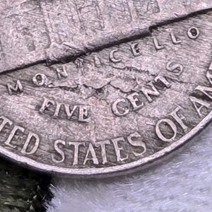 Può includere: Una moneta da cinque centesimi degli Stati Uniti color argento che raffigura l'edificio Monticello sul retro. Il testo recita MONTICELLO, FIVE CENTS e UNITED STATES OF AMERICA. La superficie metallica presenta una texture visibile.