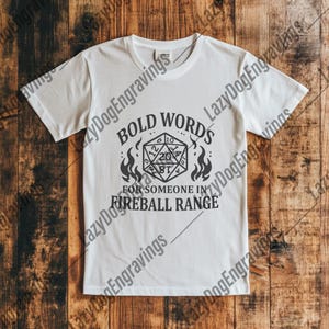 May include: White t-shirt with a black graphic of a twenty-sided die with flames on either side. The text "BOLD WORDS FOR SOMEONE IN FIREBALL RANGE" is printed below the die.