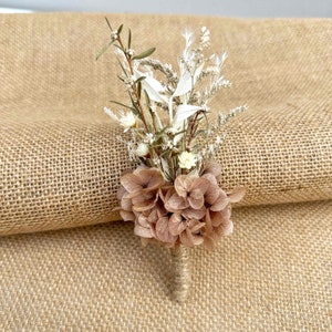 May include: A small bouquet of dried flowers featuring a brown hydrangea, white dried blooms, and green stems. The bouquet is tied with twine and is displayed on a hessian background.