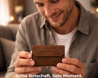 May include: A brown leather wallet with the text "Immer Dein" and a heart symbol is held by a person. The wallet has a flap closure. The text "Seine Botschaft. Sein Moment." is at the bottom of the image.