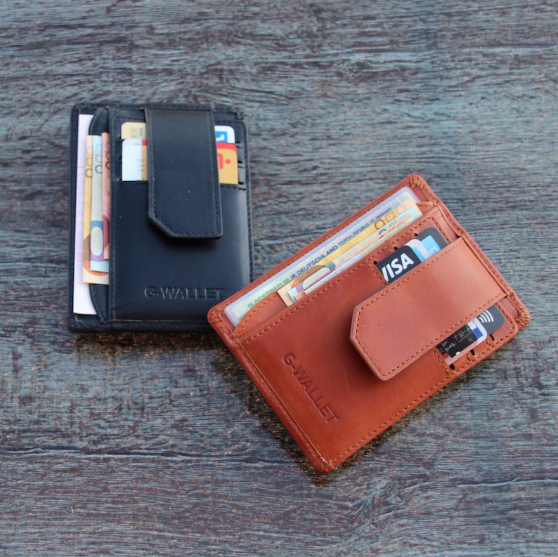Op de afbeelding: Twee G-WALLET kaarthouders, &eacute;&eacute;n in zwart en &eacute;&eacute;n in lichtbruin, elk voorzien van een verticale riemsluiting, meerdere kaartsleuven en een vak voor papiergeld. De merknaam G-WALLET is in reli&euml;f op de voorzijde van elk etui aangebracht.