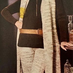 May include: A white and brown patterned knit pantsuit with a long cardigan and a black turtleneck top. The pantsuit has a brown belt.