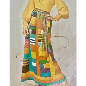 May include: A colorful patchwork maxi skirt with a variety of geometric patterns in shades of orange, yellow, green, blue, and brown. The skirt is paired with a yellow blouse and a rope belt with tassels. The skirt appears to be handmade.