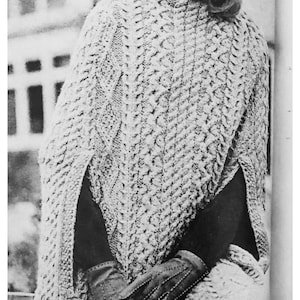 May include: A white knitted poncho with a cable knit pattern. The poncho has a high neck and a long, flowing design.