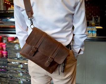 May include: A brown leather messenger bag with a long adjustable strap. The bag has two buckles on the front and a flap closure.