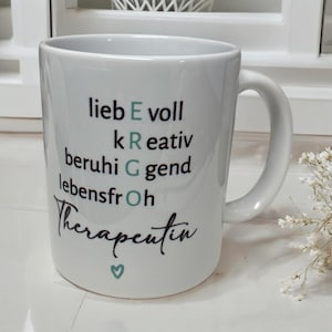 May include: White ceramic mug with a black and green design that says "lieb E voll kRativ beruhi G gend lebensfrOh  Therapentin" with a small green heart at the bottom.