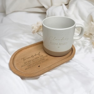 Könnte beinhalten: Ein Holz-Untersetzer mit dem Text "Freundschaft ist ein Zauber der schwere Zeiten leichter und gute Zeiten noch schöner macht" und einem Herzsymbol. Eine weiße Keramiktasse mit dem Text "Claudias kleine Auszeit" und einem Herzsymbol steht auf dem Untersetzer.