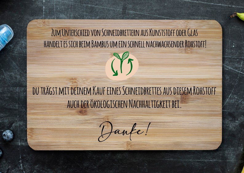 May include: A wooden cutting board with the text "ZUM UNTERSCHIED VON SCHNEIDBRETTERN AUS KUNSTSTOFF ODER GLAS HANDELT ES SICH BEIM BAMBUS UM EIN SCHNELL NACHWACHSENDER ROHSTOFF! DU TR&Auml;GST MIT DEINEM KAUF EINES SCHNEIDBRETTES AUS DIESEM ROHSTOFF AUCH DER &Ouml;KOLOGISCHEN NACHHALTIGKEIT BEI. Danke!" printed on it. The board has a light brown color and a natural wood grain.