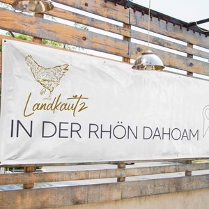 May include: White banner with a gold chicken illustration and the text "Landkautz 2 IN DER RH&Ouml;N DAHOAM" with a gold heart-shaped pin icon.