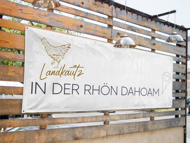 May include: White banner with a gold chicken illustration and the text "Landkautz 2 IN DER RH&Ouml;N DAHOAM" with a gold heart-shaped pin icon.