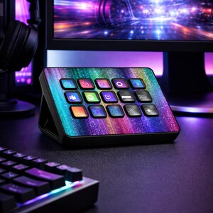 Könnte beinhalten: Ein schwarzes Streaming-Bedienfeld mit einem Regenbogen-Glitzer-Design. Das Panel hat 15 beleuchtete quadratische Tasten mit verschiedenen Symbolen. Eine Tastatur und ein Monitor befinden sich im Hintergrund.