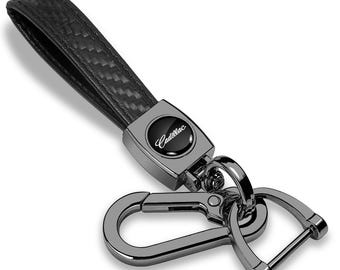 Imagen de iPick para llavero con correa de fibra de carbono negra auténtica y gancho negro metalizado, con logotipo de Cadillac Script, con licencia oficial.