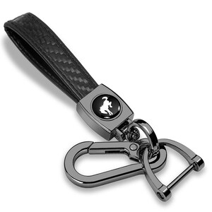 May include: Black leather keychain with a carbon fiber weave strap. The keychain features a silver-tone metal clasp and a rectangular emblem with a white horse silhouette.