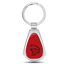 May include: A teardrop-shaped keychain with a red center and a silver border. The red center features a black graphic of a snarling cat. The keychain has a silver key ring attached at the top.