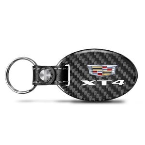 May include: Oval-shaped key chain with a carbon fiber pattern. The key chain features the Cadillac logo and the letters "XT4" in white. The key ring is attached to a black leather strap.