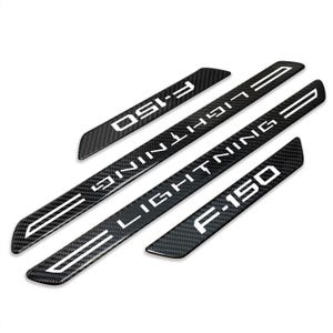 May include: Four black carbon fiber door sill protectors with white text. The text reads "F-150 LIGHTNING" on two long pieces and "F-150" on two shorter pieces. The pieces have a textured carbon fiber appearance.