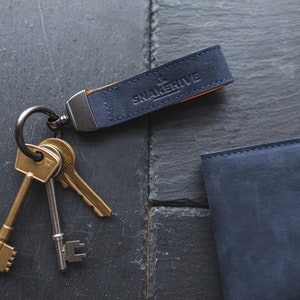 May include: A blue leather key chain with the text "Snakehive" on it. The key chain is attached to a set of three gold keys.