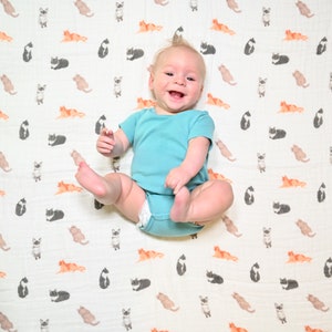 Joyful infant lying on a swaddle with a playful cat print, providing comfort and fun.