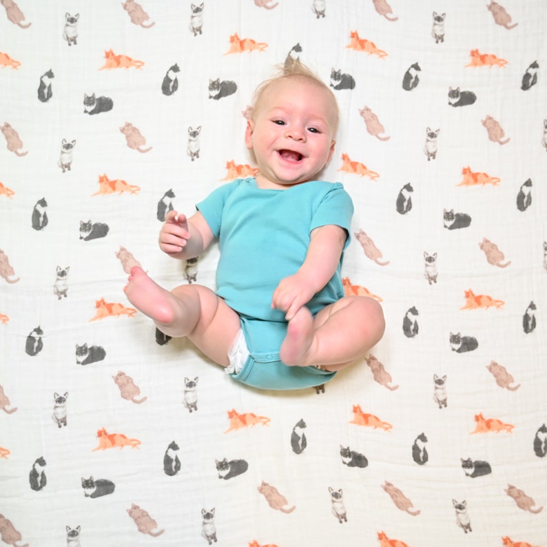 Joyful infant lying on a swaddle with a playful cat print, providing comfort and fun.