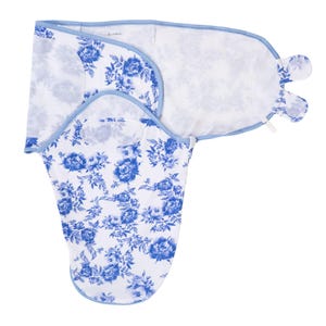 May include: A white baby swaddle blanket with a blue floral pattern. The swaddle has a light blue trim and a unique design for secure wrapping. The floral print features detailed blue flowers and leaves, creating a classic and elegant look.