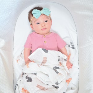 Baby with a charming bow looks curious and cozy wrapped in a cat-themed swaddle.