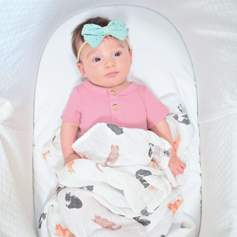 Baby with a charming bow looks curious and cozy wrapped in a cat-themed swaddle.