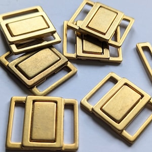 Eine kleine moderne Metallschnalle aus goldfarbenen Metall, für Riemen und Gürtel zum Annähen, 2-teilig, 20 x 23 mm