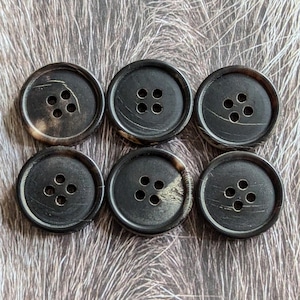 Puede incluir: Seis botones de cuerno negros y marrones con cuatro agujeros cada uno.