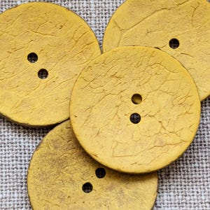 May include: Four yellow round buttons with a textured surface and two holes each. The buttons are made of wood and have a distressed look.