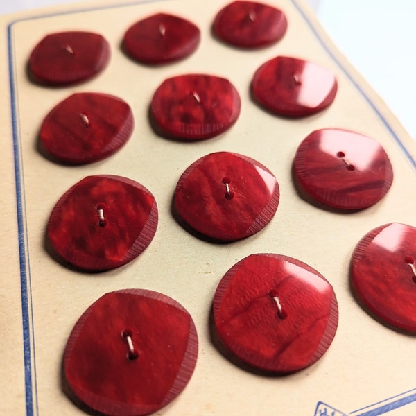 12 alte Kunststoffknöpfe auf einer Knopfkarte, leuchtend rot, meliert, dezentes Ziermuster am Rand, 27 mm