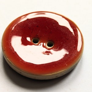 Könnte beinhalten: Ein roter Keramikknopf mit zwei Löchern. Der Knopf hat eine glänzende Oberfläche.
