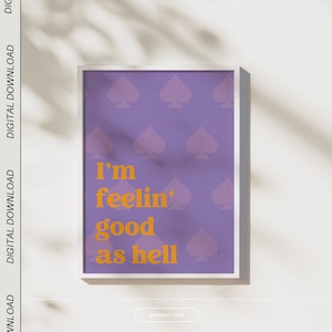Può includere: Una stampa artistica incorniciata con sfondo viola e simboli di picche ripetuti. La stampa presenta il testo "I'm feelin' good as hell" in arancione. La cornice è bianca e l'estetica generale è moderna e minimalista.