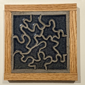 May include: A framed ceramic tile with a dark blue background and a raised, white design of a maze or labyrinth.